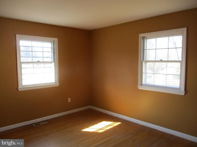 spare room featuring wood finished floors, visible vents, and baseboards