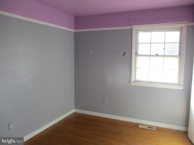 spare room featuring plenty of natural light, wood finished floors, visible vents, and baseboards