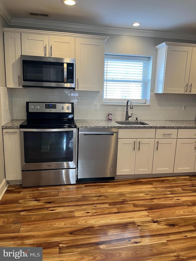 kitchen featuring light stone counters, crown molding, appliances with stainless steel finishes, a sink, and wood finished floors