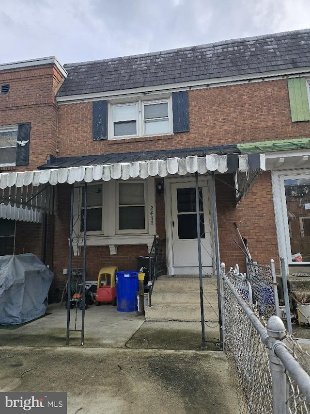 townhome / multi-family property featuring brick siding, mansard roof, a shingled roof, entry steps, and fence