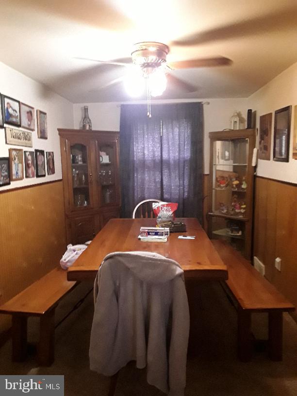 dining room with a wainscoted wall, a ceiling fan, and wooden walls