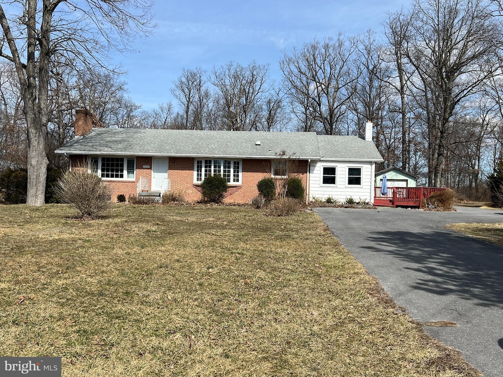 ranch-style house featuring aphalt driveway, a front yard, brick siding, and a chimney