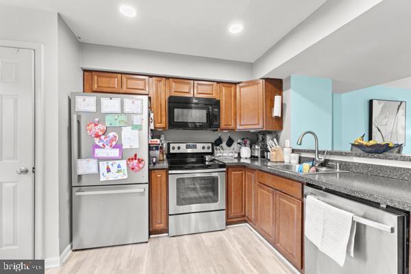 kitchen with dark countertops, light wood-type flooring, appliances with stainless steel finishes, and a sink