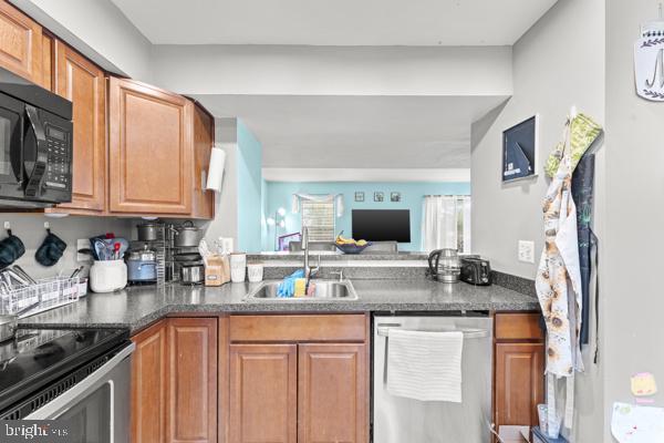 kitchen with black microwave, stainless steel dishwasher, dark countertops, and a sink