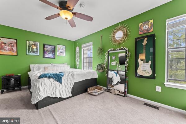 bedroom featuring baseboards, visible vents, a ceiling fan, an accent wall, and carpet flooring