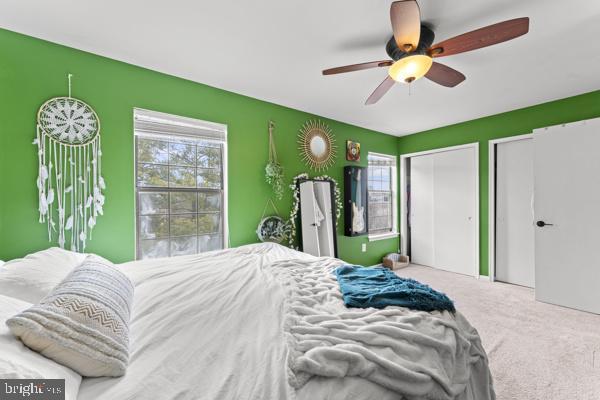 carpeted bedroom featuring a ceiling fan and two closets