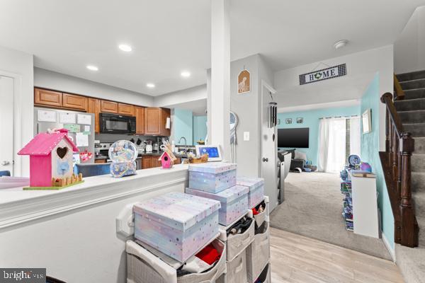 kitchen featuring brown cabinetry, open floor plan, fridge, black microwave, and recessed lighting