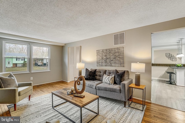 living room with baseboards, a textured ceiling, visible vents, and hardwood / wood-style floors