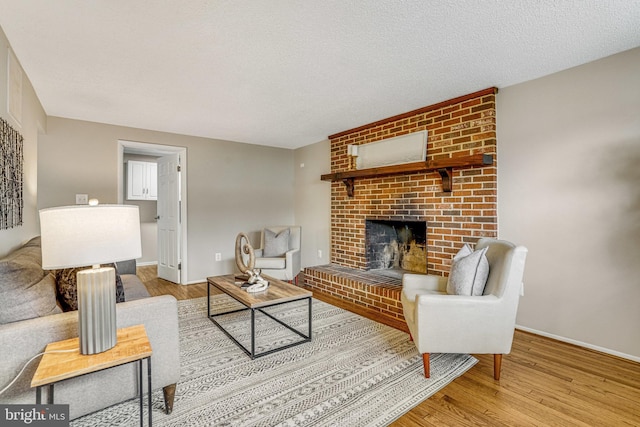 living area with a brick fireplace, a textured ceiling, baseboards, and wood finished floors