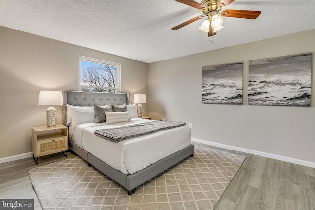 bedroom featuring ceiling fan, light wood-style flooring, baseboards, and a textured ceiling