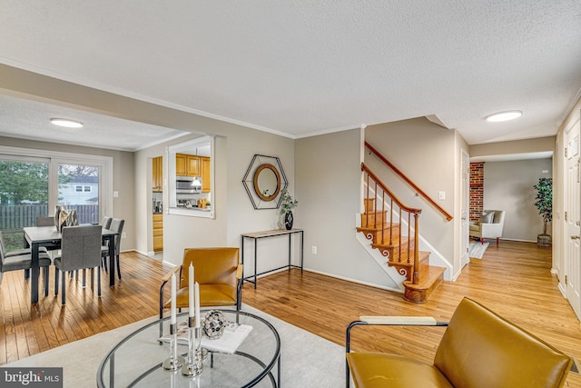 living room featuring light wood-style flooring, ornamental molding, stairway, and a textured ceiling