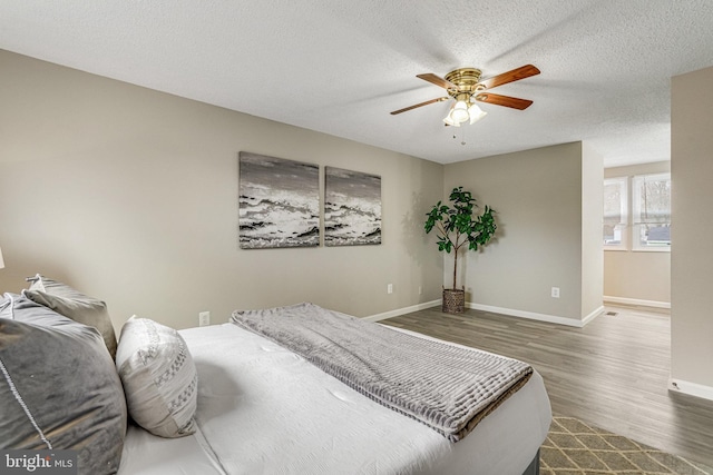 bedroom with a textured ceiling, ceiling fan, dark wood-style flooring, and baseboards