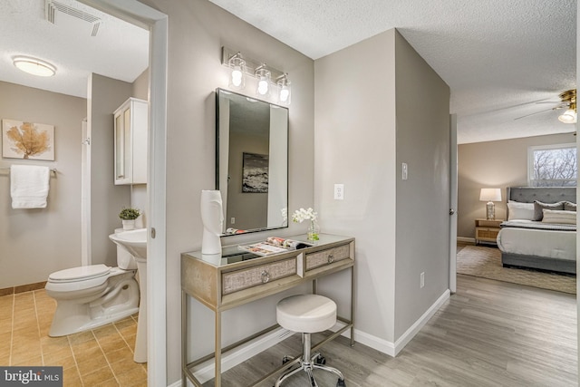 bathroom with toilet, a textured ceiling, visible vents, and baseboards