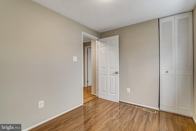 unfurnished bedroom with a textured ceiling, a closet, wood finished floors, and baseboards