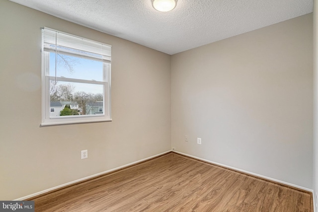 empty room with a textured ceiling, baseboards, and wood finished floors