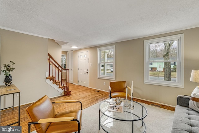 living room featuring a textured ceiling, wood finished floors, baseboards, ornamental molding, and stairway