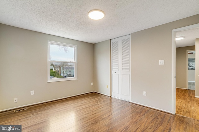 unfurnished bedroom featuring a closet, visible vents, a textured ceiling, baseboards, and hardwood / wood-style flooring