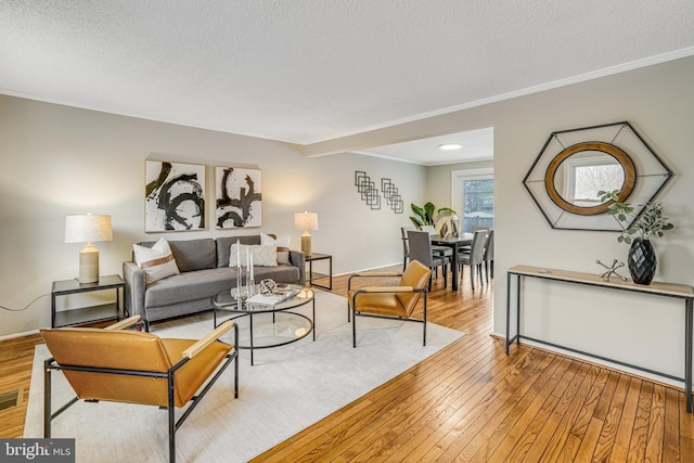 living room with a textured ceiling, hardwood / wood-style flooring, visible vents, baseboards, and ornamental molding