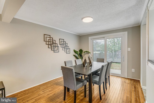 dining space with light wood-style floors, baseboards, ornamental molding, and a textured ceiling