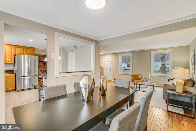 dining area featuring a textured ceiling, light wood finished floors, stairway, and crown molding