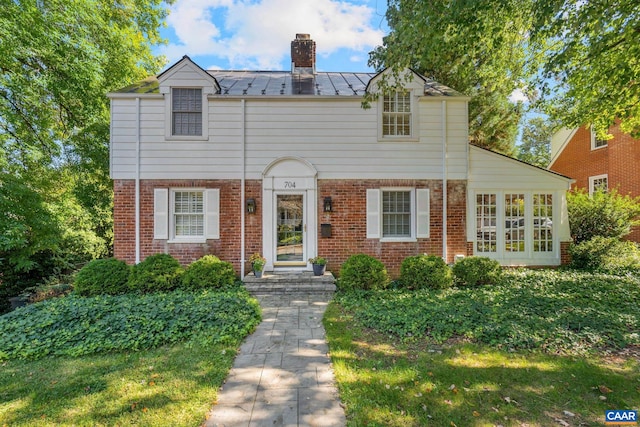 view of front of house featuring a standing seam roof, brick siding, metal roof, and a chimney