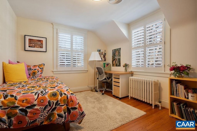 bedroom featuring radiator, multiple windows, vaulted ceiling, and wood finished floors