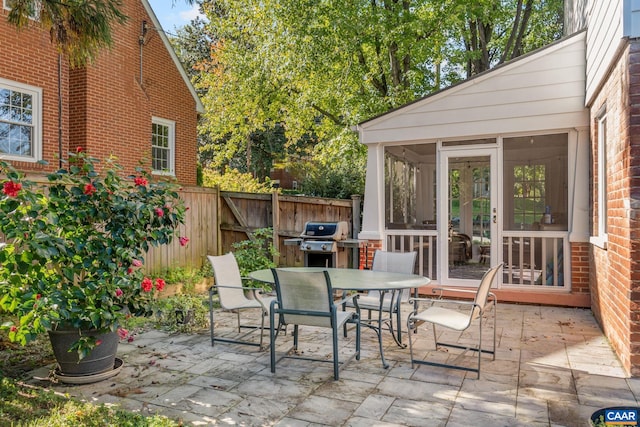 view of patio with outdoor dining space, a sunroom, and fence