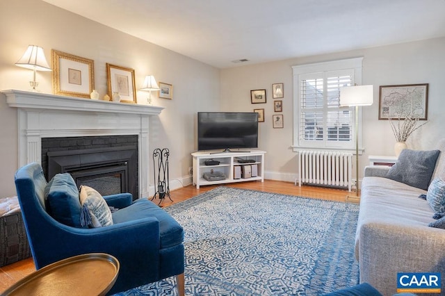 living area featuring a fireplace, wood finished floors, visible vents, baseboards, and radiator heating unit