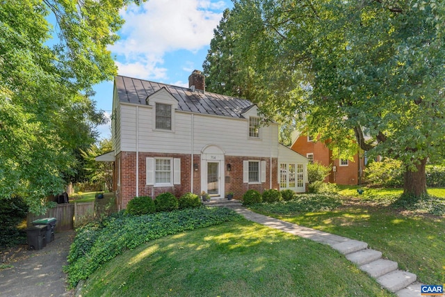 view of front of property featuring brick siding, a chimney, metal roof, a standing seam roof, and a front yard