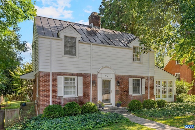 view of front facade with a standing seam roof, brick siding, metal roof, and a chimney