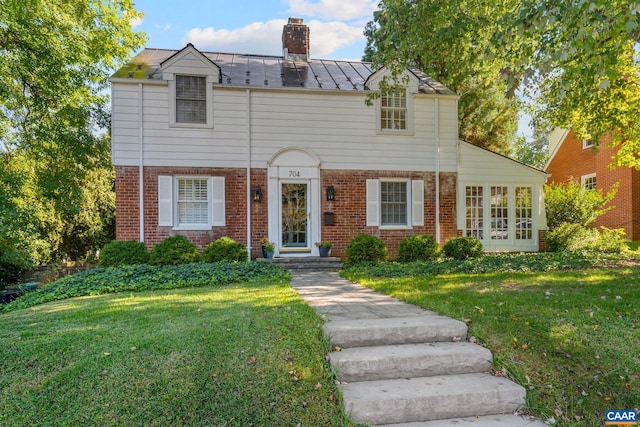 view of front facade featuring a chimney, metal roof, a standing seam roof, a front lawn, and brick siding