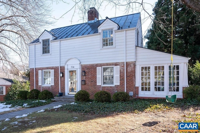 view of front of house with a standing seam roof, a chimney, metal roof, and brick siding