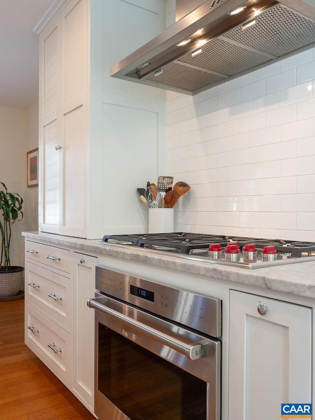 kitchen with stainless steel appliances, wall chimney range hood, backsplash, and white cabinets