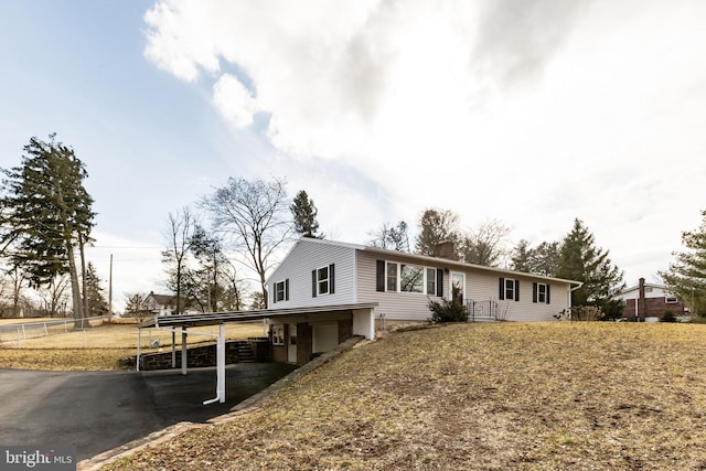 single story home with aphalt driveway, a chimney, an attached garage, fence, and a carport