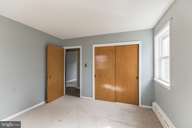 unfurnished bedroom with a baseboard heating unit, a closet, carpet floors, and baseboards