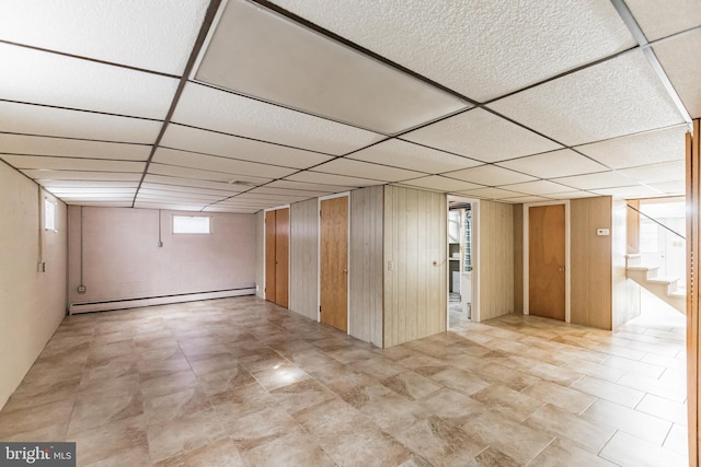 below grade area with a paneled ceiling, wooden walls, stairway, and baseboard heating