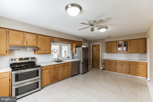 kitchen with brown cabinets, stainless steel appliances, light countertops, under cabinet range hood, and a sink