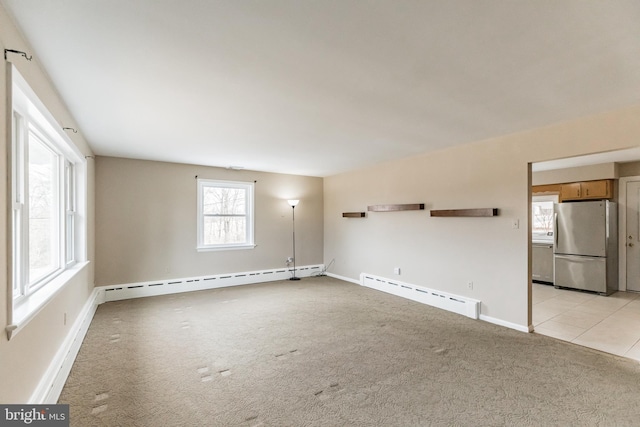 empty room featuring a baseboard heating unit, light carpet, baseboards, and light tile patterned floors