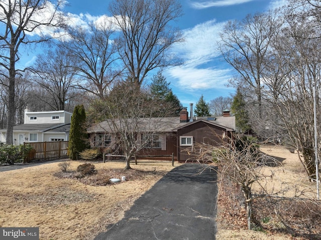 ranch-style house with driveway, a chimney, and fence