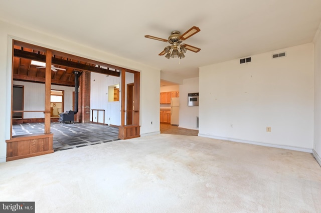 spare room featuring ceiling fan, visible vents, carpet, and a wood stove