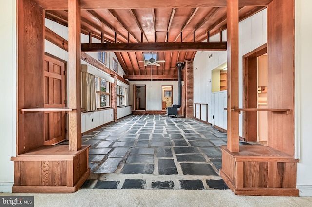 interior space with wood ceiling, wooden walls, a wood stove, and a ceiling fan