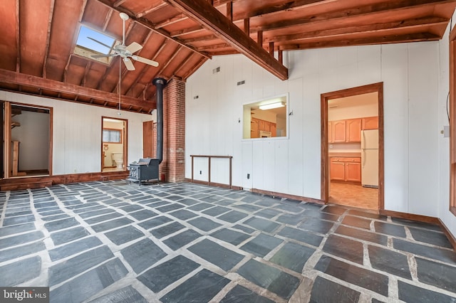 unfurnished living room featuring a wood stove, lofted ceiling with skylight, baseboards, and a ceiling fan