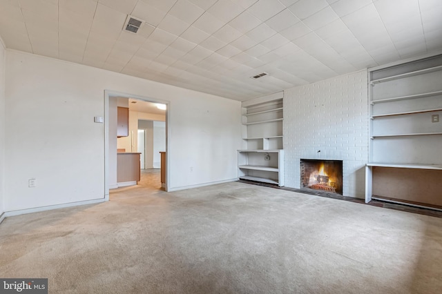 unfurnished living room with built in shelves, a brick fireplace, carpet flooring, and visible vents