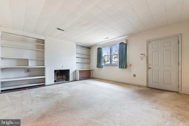 unfurnished living room featuring a brick fireplace, carpet, visible vents, and built in features