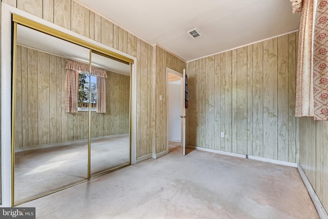 unfurnished bedroom with a closet, visible vents, carpet flooring, wood walls, and baseboards