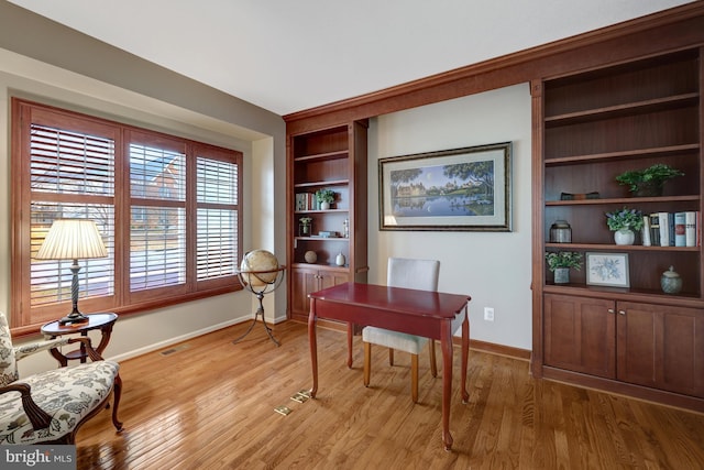 home office featuring visible vents, built in features, baseboards, and light wood-type flooring