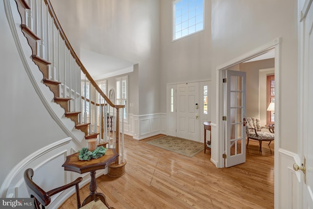 foyer with stairway, a high ceiling, wainscoting, a decorative wall, and light wood-type flooring