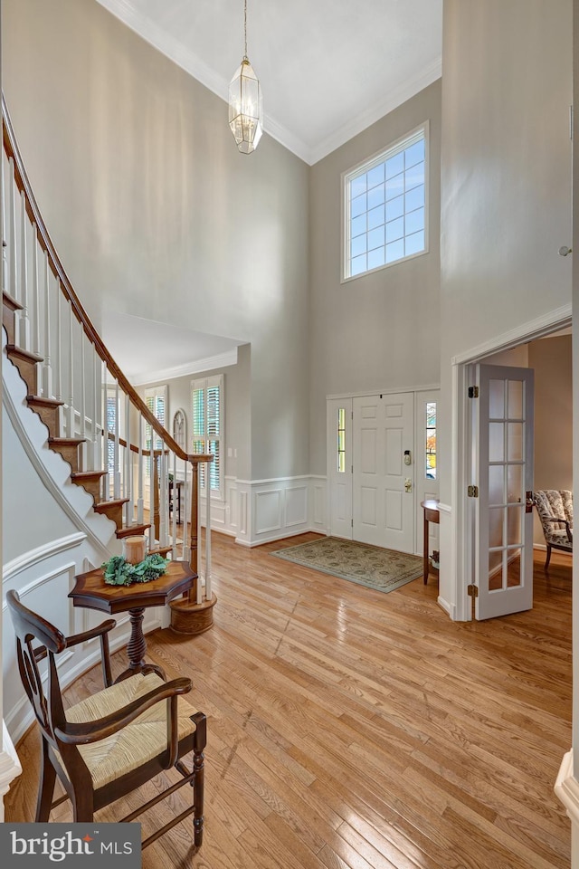 foyer entrance with a wainscoted wall, stairs, ornamental molding, light wood-style flooring, and a notable chandelier