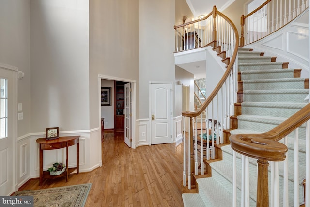 entrance foyer featuring wood finished floors, stairway, a high ceiling, wainscoting, and a decorative wall