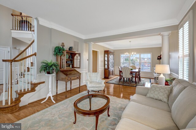 living area featuring stairway, wood finished floors, an inviting chandelier, decorative columns, and ornamental molding